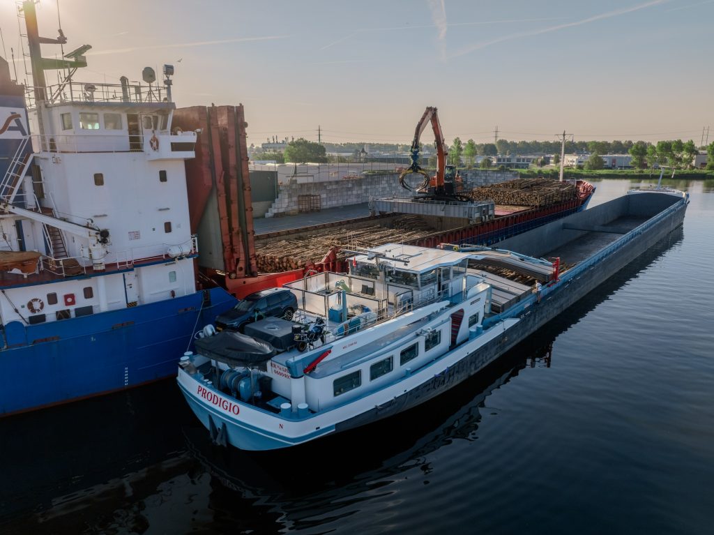 Binnenvaartschip langszij een zeeschip tijdens de overslag van hout