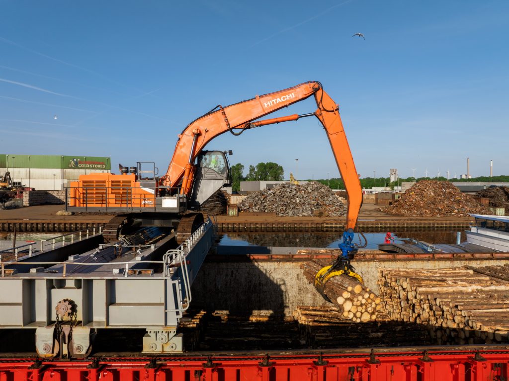 Kraan met houtgrijper boven een lading boomstammen